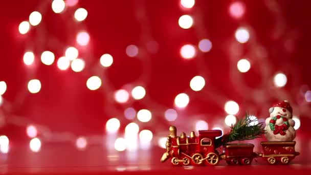 Treno giocattolo di Natale con un pupazzo di neve e un albero di Natale si muove su uno sfondo di colore rosso e una ghirlanda scintillante — Video Stock