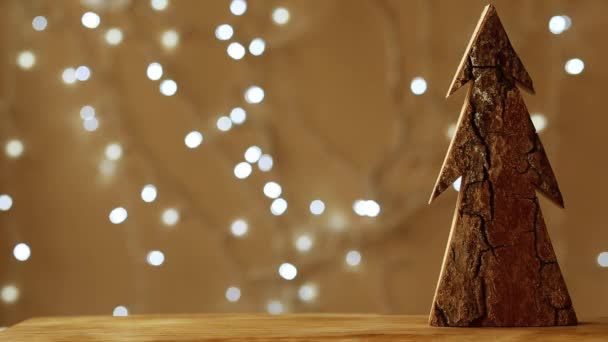 Albero di Natale in legno fatto a mano si erge su uno sfondo marrone. ghirlanda di Natale brilla sullo sfondo — Video Stock