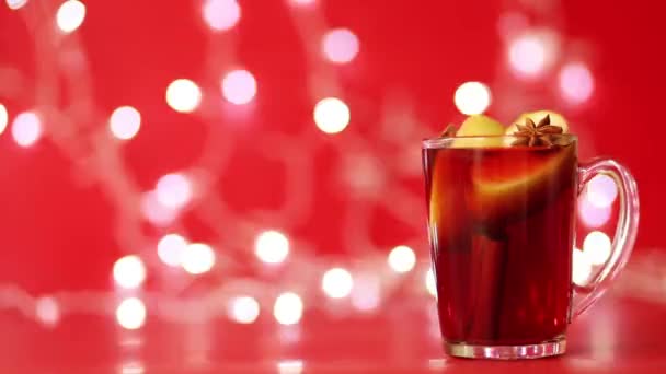 Ett glas glögg gjort av rött vin står mot bakgrund av röda och mousserande kransar — Stockvideo