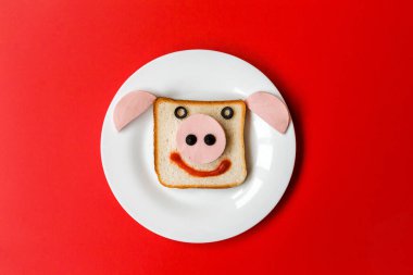 Beyaz tabakta boğa kafası şeklinde bir sandviç. Plaka kırmızı arka planda duruyor. Yatay fotoğraf