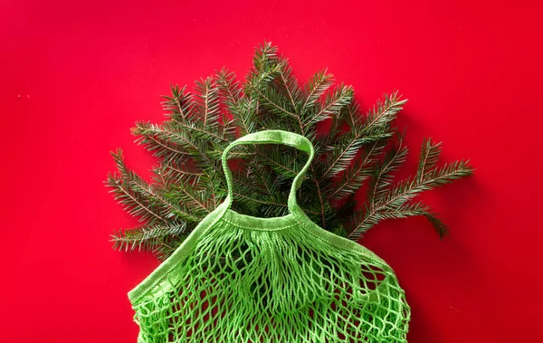 Mesh green cotton bag with Christmas fir tree branches and red background. Zero waste. Eco friendly Xmas. view from above. Horizontal photo
