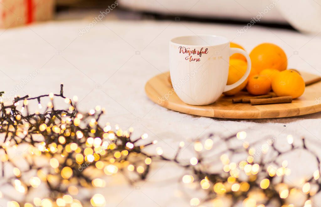 A white cup with the inscription Wonderful Winter stands on a wooden tray, pallesins and cinnamon lie next to it. The tray is on a soft white carpet. Horizontal photo