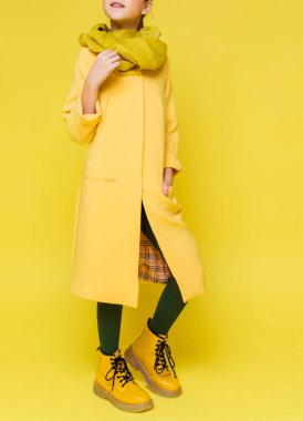 Sarı ceketli, atkılı, yeşil taytlı ve sarı çizmeli şık bir genç kız. Dikey fotoğraf