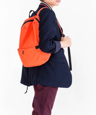 Omzunda turuncu bir çanta olan bir okul çocuğunun fotoğrafı okul üniforması içinde beyaz bir arkaplanda duruyor. Pantolon, ceket ve gömlek..