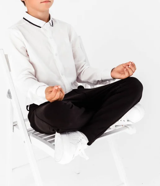 身穿白色衬衫和黑色长裤的男孩在白色的背景上摆设着一个莲花的姿势 学生放松和冥想 — 图库照片