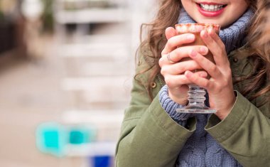 Yeşil ceketli ve elinde bir bardak sıcak çikolatayla poz veren mavi kazaklı bir kız. Fotoğraf.