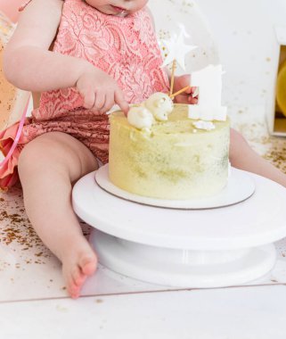 Pembe takım elbiseli küçük bir kız, bir şenlik dekorasyonunun arka planında elleri ile pasta yiyor. Fotoğraf.