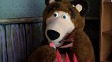 Kahverengi ayının gerçek boyutlarda bir kuklası rahat bir koltukta oturur ve şeker yer. Yüksek kaliteli FullHD görüntüler. Minsk, Belarus - 5 Eylül 2021