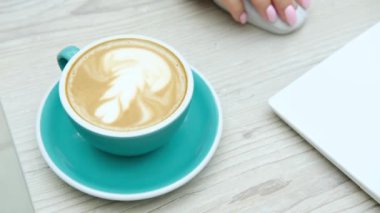 Kahve molası. Bilgisayarda yazı yazan bir kadınla çalışma masasında bir fincan cappuccino. Yüksek kalite 4k görüntü