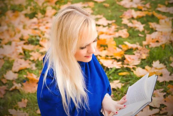 Blonde vrouw lezen van een boek in de herfst park. — Stockfoto