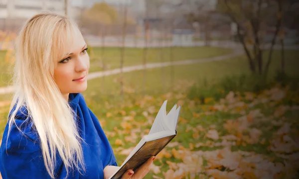 金发女人片秋色的公园里看书. — 图库照片