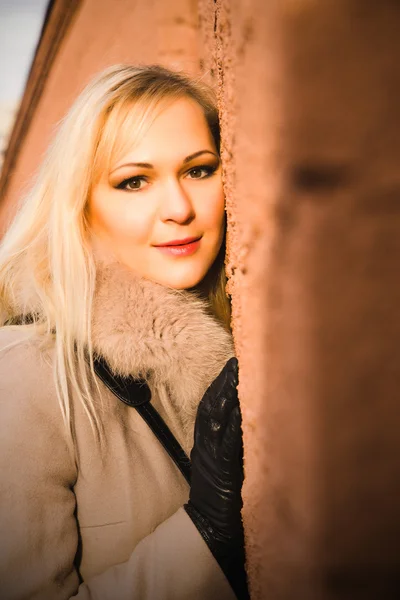 Portrait of blonde girl in warm coat over a brick wall — Stock Photo, Image