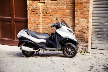Motorlu scooter bir bina duvarın önünde park etmiş.
