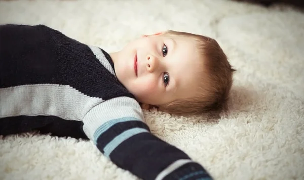 Ein glücklicher kleiner Junge ruht auf dem weißen Teppich — Stockfoto