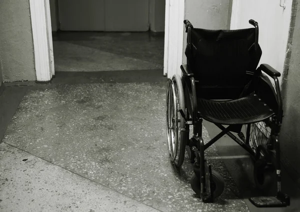 Cadeira de rodas velha em pé em um corredor vazio. Preto e branco pho — Fotografia de Stock