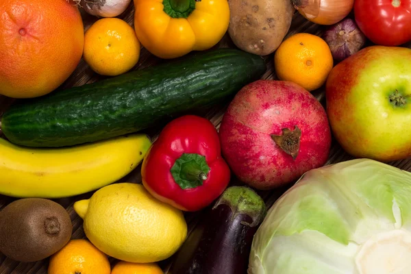 a variety of vegetables and fruits, onion, cucumber, cabbage, tomatoes, peppers, eggplant, apples, bananas, oranges, kiwi, lemon on the wooden background
