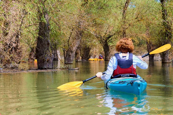 Sel basmış ağaçların arasında mavi kanolu bir kadın. Tuna Nehri 'nin ıssız bölgelerinde kayak yapmak ormandaki sel basmış ağaçların arasında Tuna Biyosferi' nin yüksek sularında.