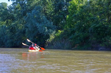 İki kadın Tuna nehrinde sarı bir kano sürüyor. İlkbaharda su turizmi ve eğlence