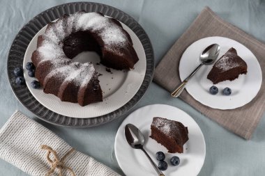 Ev yapımı vejetaryen çikolatalı pasta, üzerine pudra şekeri serpiştirilmiş. Yabanmersini ve tatlı tabakları. Kopyalama alanı olan üst görünüm. Seçici odak.