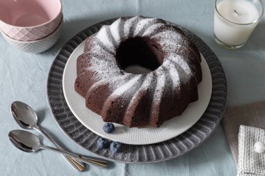 Ev yapımı vejetaryen çikolatalı pasta, üzerine pudra şekeri serpiştirilmiş. Yabanmersini ve tatlı tabakları. Kopyalama alanı olan üst görünüm. Seçici odak.
