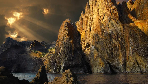 Fantasy on the theme of rocky cliffs on the seashore. The rays of the sun, through the moody clouds, illuminate the mountains