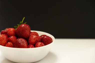 Siyah arka planda beyaz bir kasede taze olgun çilek içeren minimalist bir kompozisyon. Modern gıda tasarımı, reklamcılık, temiz markalaşma ve sağlıklı yaşam tarzı içeriği için ideal.