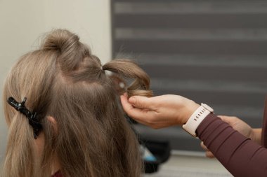 Yetişkin bir kadının saçında saç maşası kullanan bir kuaförün yakın görüntüsü. Profesyonel saç şekillendirme, güzellik ve kuaför aletleri kavramı.