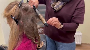 Kuaför, genç bir kızın saçına şekil verdikten sonra bitişik kıvırcık saçı nazikçe salıyor. Profesyonel kuaförlük, çocuklara saç bakımı ve güzellik salonu hizmetleri kavramı.