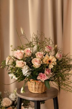 Hasır sepetteki doğal buket rahat bir atmosfer yaratıyor. Sıcak iç ışıkta güller ve yeşilliklerle taşralı çiçek sepeti