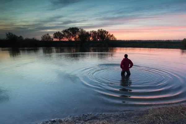 The man costs in the small river and admires a decline. — Stock Photo, Image