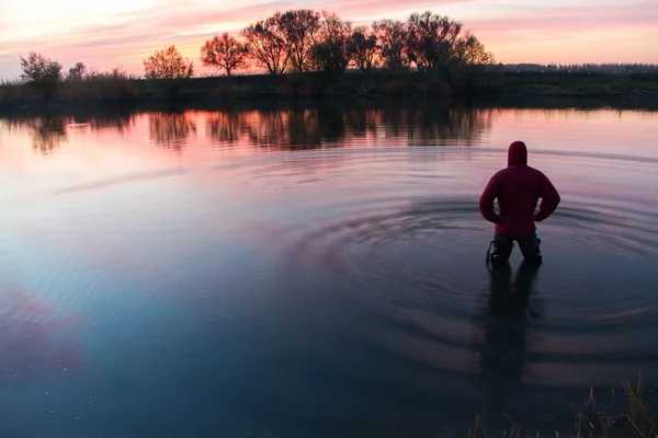 The man costs in the small river and admires a decline. — Stock Photo, Image