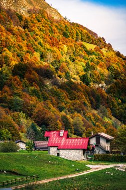 İtalya 'nın Julian Alpleri' nde bulunan Resia Vadisi 'ndeki manzara. Canlı sonbahar yaprakları ve yeşil çimenli yamaçlara kurulmuş birkaç küçük geleneksel ev..
