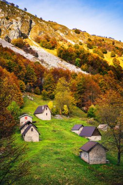 İtalya 'nın Julian Alpleri' nde bulunan Resia Vadisi 'ndeki manzara. Canlı sonbahar yaprakları ve yeşil çimenli yamaçlara kurulmuş birkaç küçük geleneksel ev..
