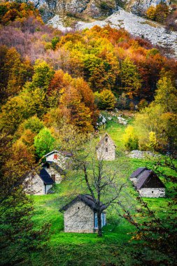 İtalya 'nın Julian Alpleri' nde bulunan Resia Vadisi 'ndeki manzara. Canlı sonbahar yaprakları ve yeşil çimenli yamaçlara kurulmuş birkaç küçük geleneksel ev..