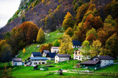 İtalya 'nın Julian Alpleri' nde bulunan Resia Vadisi 'ndeki manzara. Canlı sonbahar yaprakları ve yeşil çimenli yamaçlara kurulmuş birkaç küçük geleneksel ev..