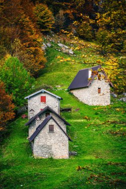 İtalya 'nın Julian Alpleri' nde bulunan Resia Vadisi 'ndeki manzara. Canlı sonbahar yaprakları ve yeşil çimenli yamaçlara kurulmuş birkaç küçük geleneksel ev..