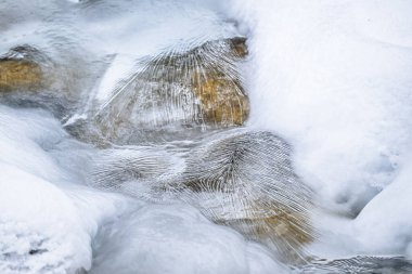 Water flowing over snowy rocky surface in winter mountains