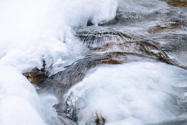 Water flowing over snowy rocky surface in winter mountains