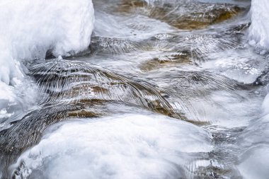 Water flowing over snowy rocky surface in winter mountains