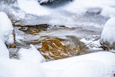 Water flowing over snowy rocky surface in winter mountains