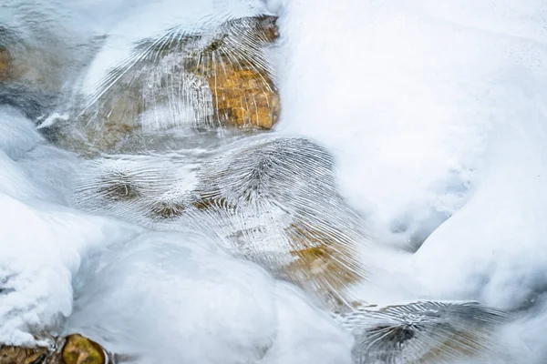 Water flowing over snowy rocky surface in winter mountains