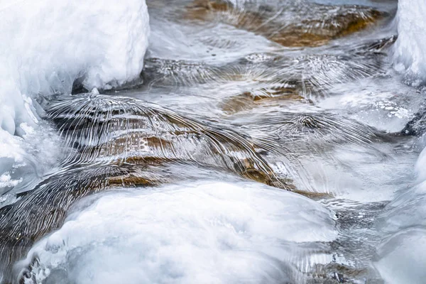 Water flowing over snowy rocky surface in winter mountains