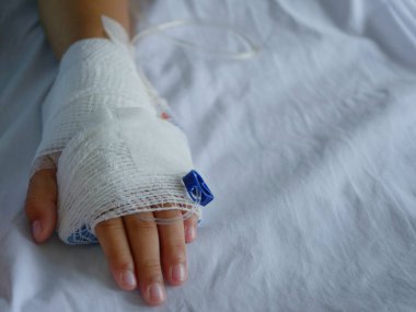 Hastanın eli beyaz bandajlara sarılı ve serum fizyolojik serumu var..