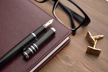 İş amaçlı aksesuarları üstünde okul sırası: Not Defteri, günlük, dolma kalem, kol düğmeleri, gözlük. 