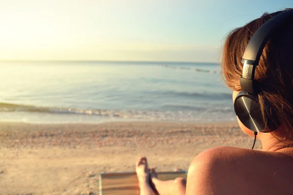 Young woman in headphones listening music and enjoying beautiful views sea, rear view. — Stock Photo, Image
