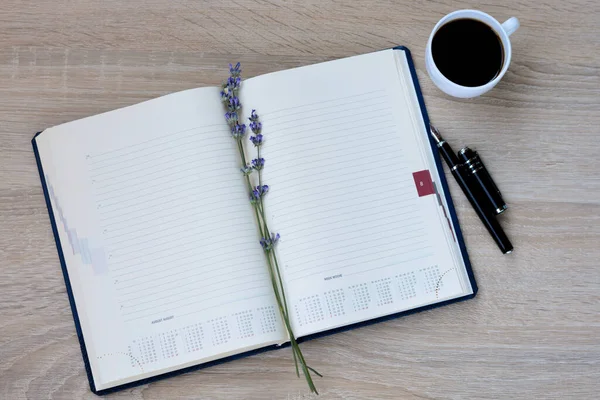 Notepad (diary), pen, flowers (lavender) and a cup of coffee on a wooden background.