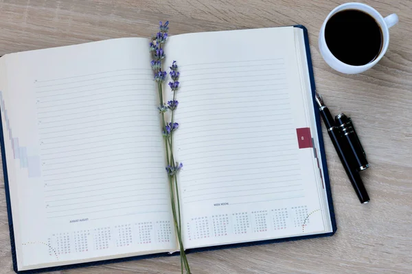 Notepad (diary), pen, flowers (lavender) and a cup of coffee on a wooden background.