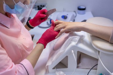 Bir kadın masaya oturur ve müşteriye manikür yapar. Pembe cüppeli bir manikür ustası.