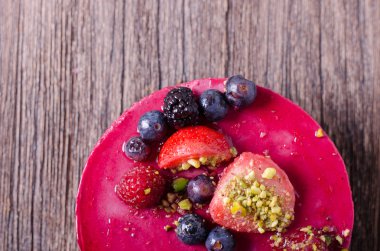 Taze çilek, ahududu, yaban mersini, kuş üzümü ve ahşap zemin üzerine Antep fıstığı ile lezzetli frambuazlı pasta. metniniz için boş alan.