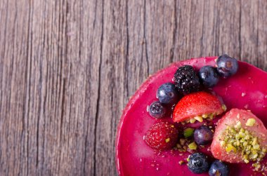 Taze çilek, ahududu, yaban mersini, kuş üzümü ve ahşap zemin üzerine Antep fıstığı ile lezzetli frambuazlı pasta. metniniz için boş alan.